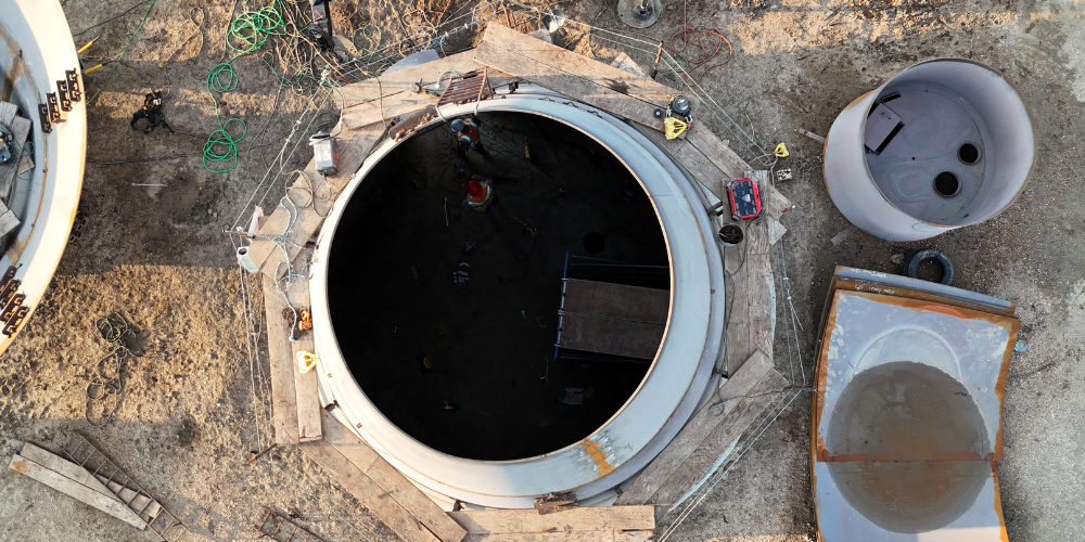 Top-down view of a circular concrete tank under construction with a worker inside and precast components nearby.