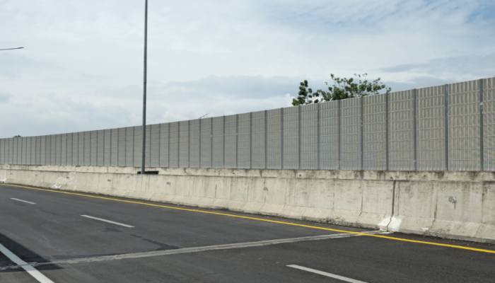 A curved highway lined with tall, gray noise‑barrier walls and streetlights under a partly cloudy sky.